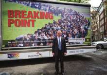 A photograph of politician Nigel Farage standing in front of a large mobile billboard for the 2016 Brexit campaign. The billboard features the prominent red headline "BREAKING POINT" and the subtitle "The EU has failed us all," set against a background showing a long, dense column of migrants and refugees walking along a road.